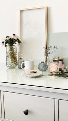 A minimalist vignette featuring rovance accessories arranged on a white wooden table with soft pink accents