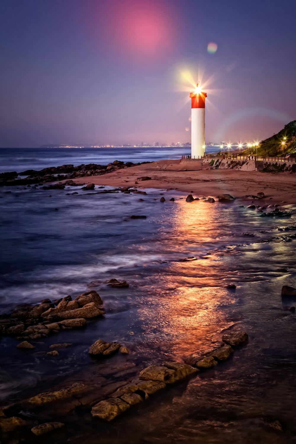 Faro blanco y rojo en la orilla del mar durante la puesta de sol