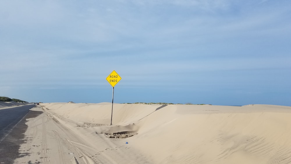 yellow and black road sign on white sand