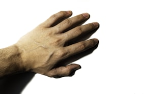 A human hand with outstretched fingers placed against a plain white background, showing details of the skin texture and veins.