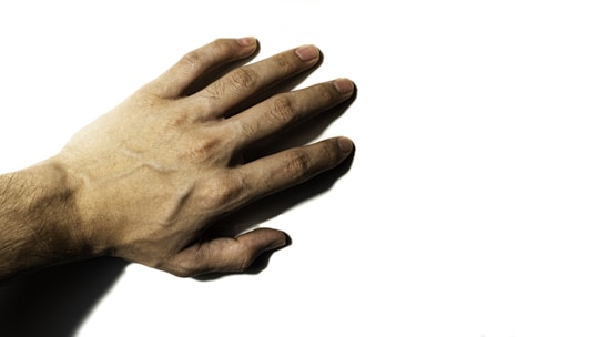 A human hand with outstretched fingers placed against a plain white background, showing details of the skin texture and veins.