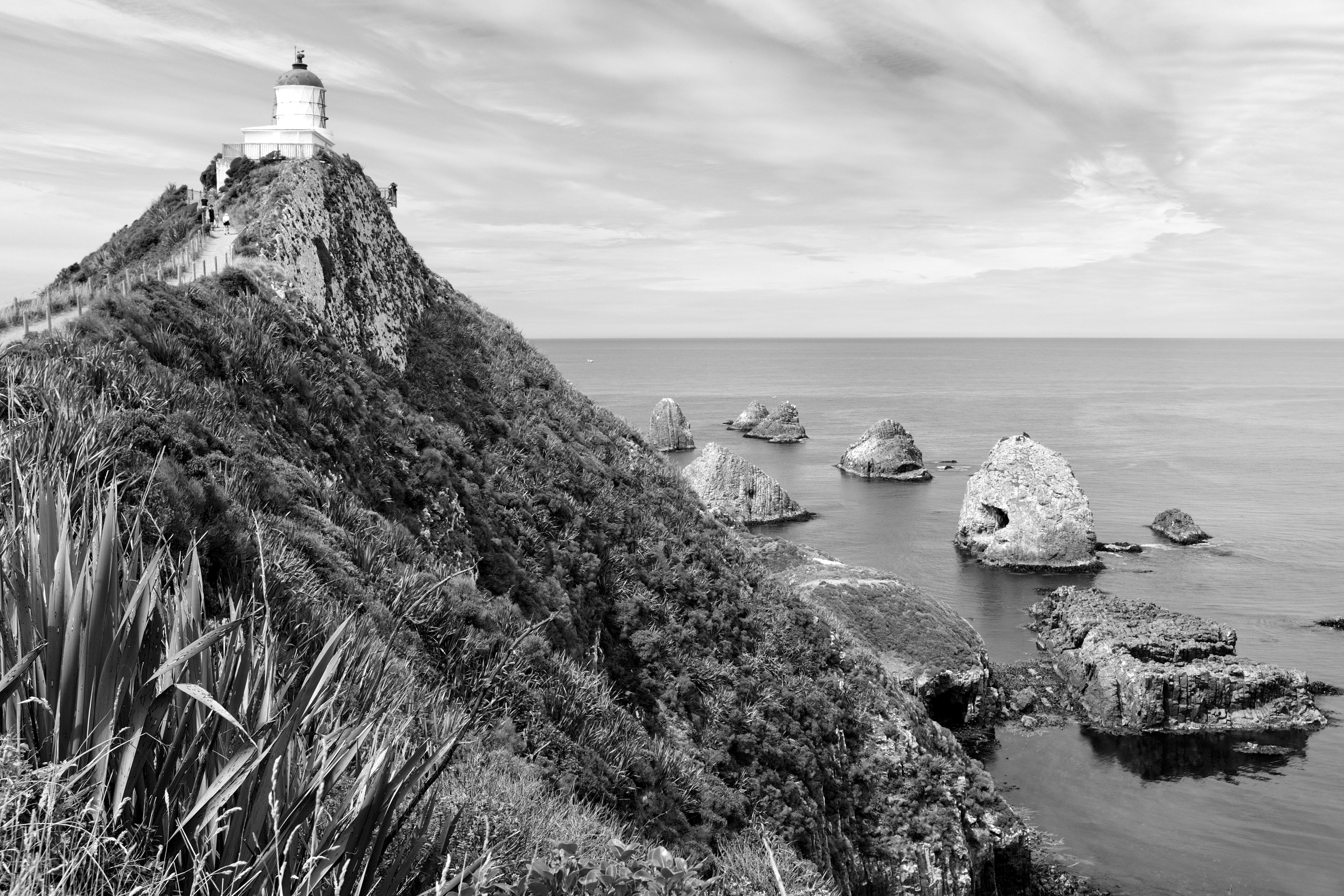 grayscale photo of lighthouse on rock formation near body of water