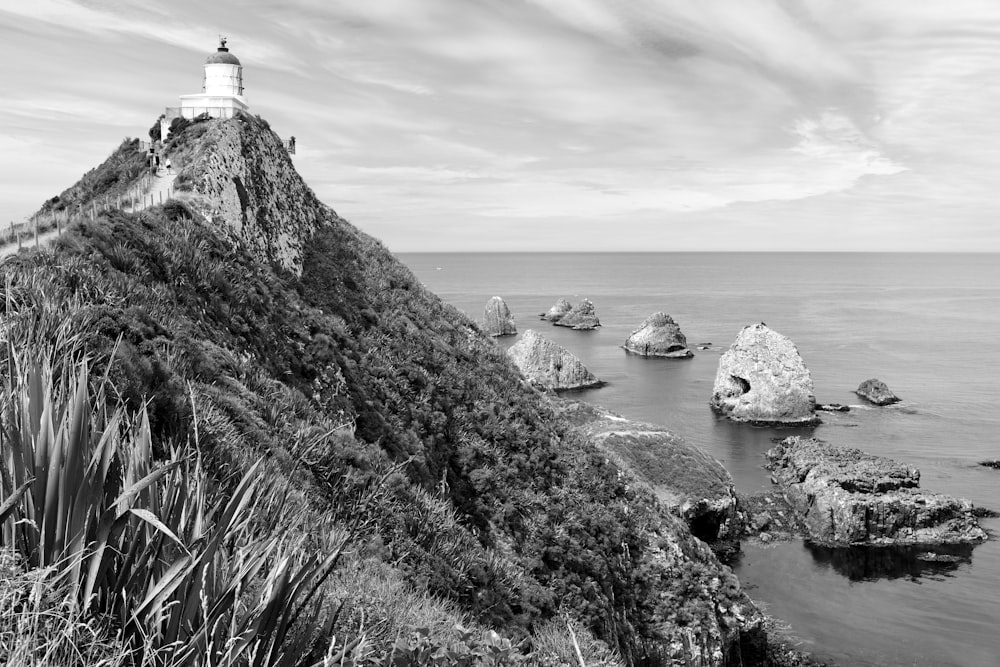 grayscale photo of lighthouse on rock formation near body of water