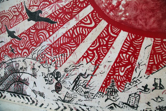 A colorful mural featuring a large red circle, possibly representing a sun, with radiating red and white patterns. The mural includes silhouettes of birds flying overhead and various buildings and cityscape elements drawn in black with intricate designs. Waves and abstract elements interweave throughout the depiction.