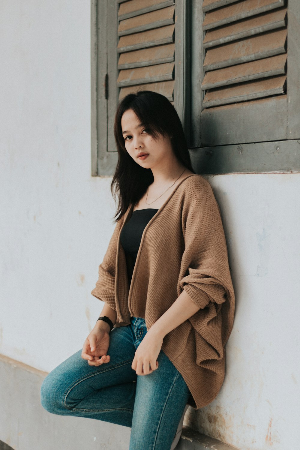 woman in brown cardigan and blue denim jeans sitting on blue concrete bench