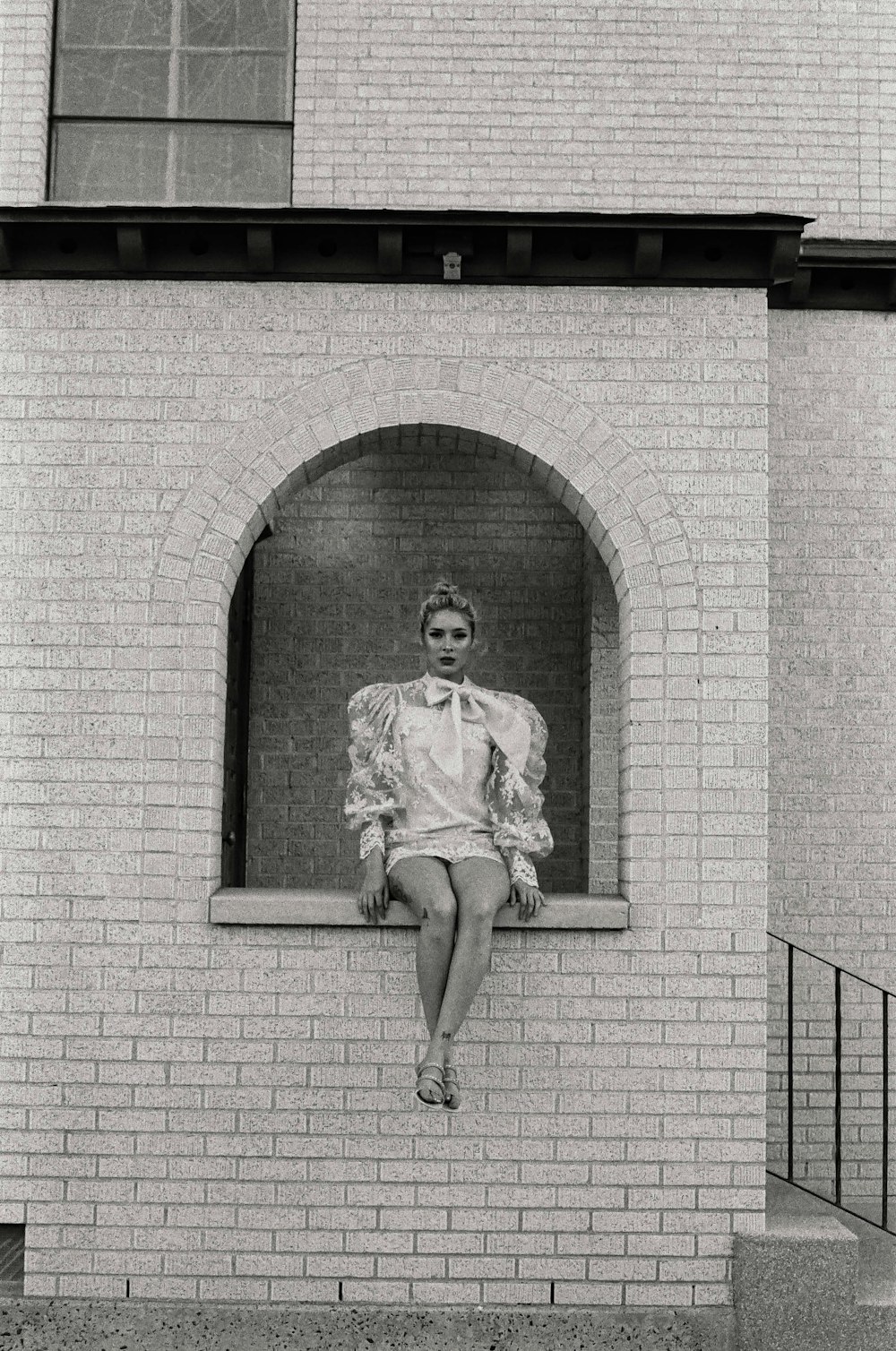 grayscale photo of man in dress shirt and pants leaning on brick wall
