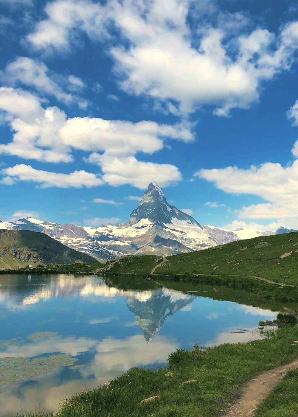 Montagna innevata vicino al lago sotto il cielo blu e le nuvole bianche durante il giorno