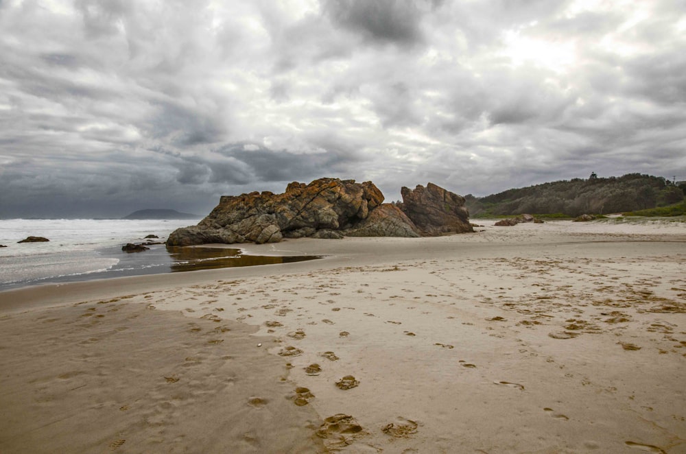 brown rock formation on sea shore under white clouds during daytime