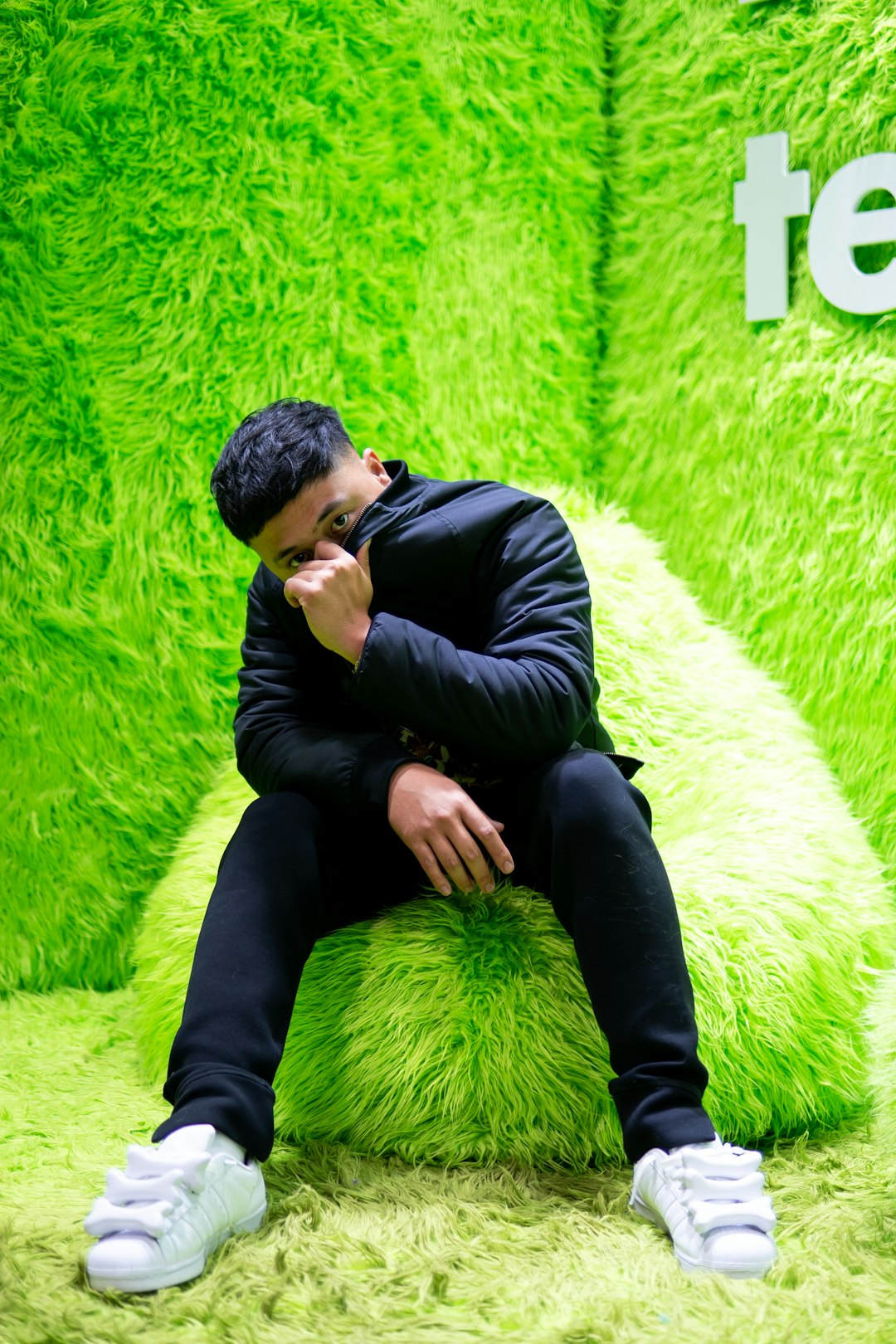 man in black long sleeve shirt and black pants sitting on green fur textile