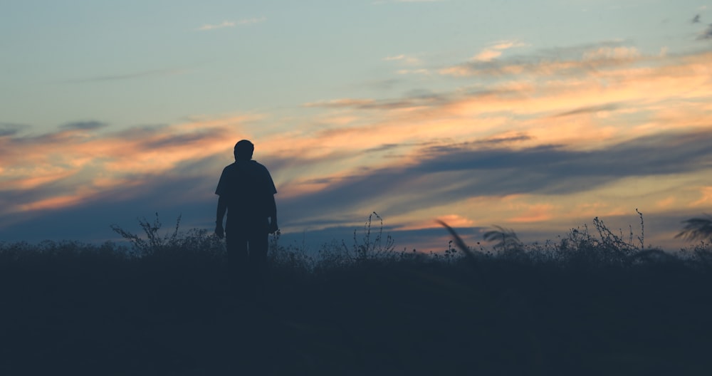 silhouette of man and woman standing on grass field during sunset