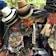 A vibrant display of assorted items, including neatly stacked hats of various materials and colors, colorful alphabet beads, decorative hair accessories, jewelry, and fabric belts. The collection appears densely packed and visually stimulating, likely part of a market stall.