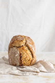 A rustic loaf of bread with a golden crust resting on a cream-colored cloth.