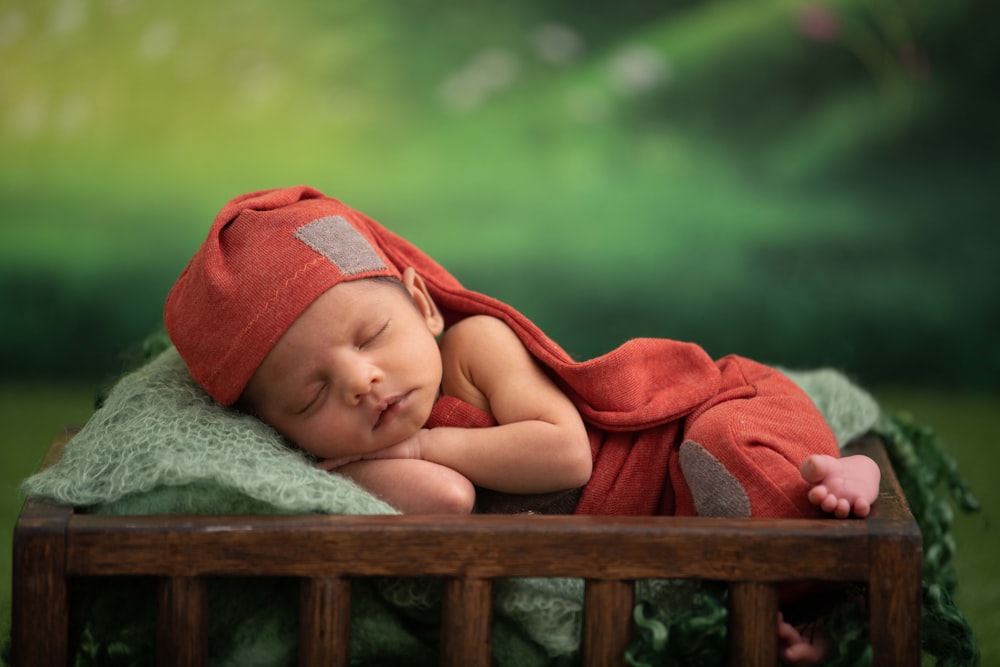 baby in red blanket lying on green textile