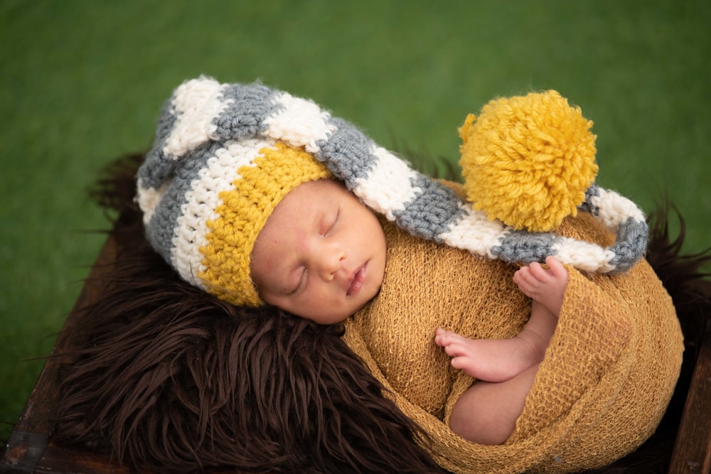 baby in white and black knit cap lying on brown textile