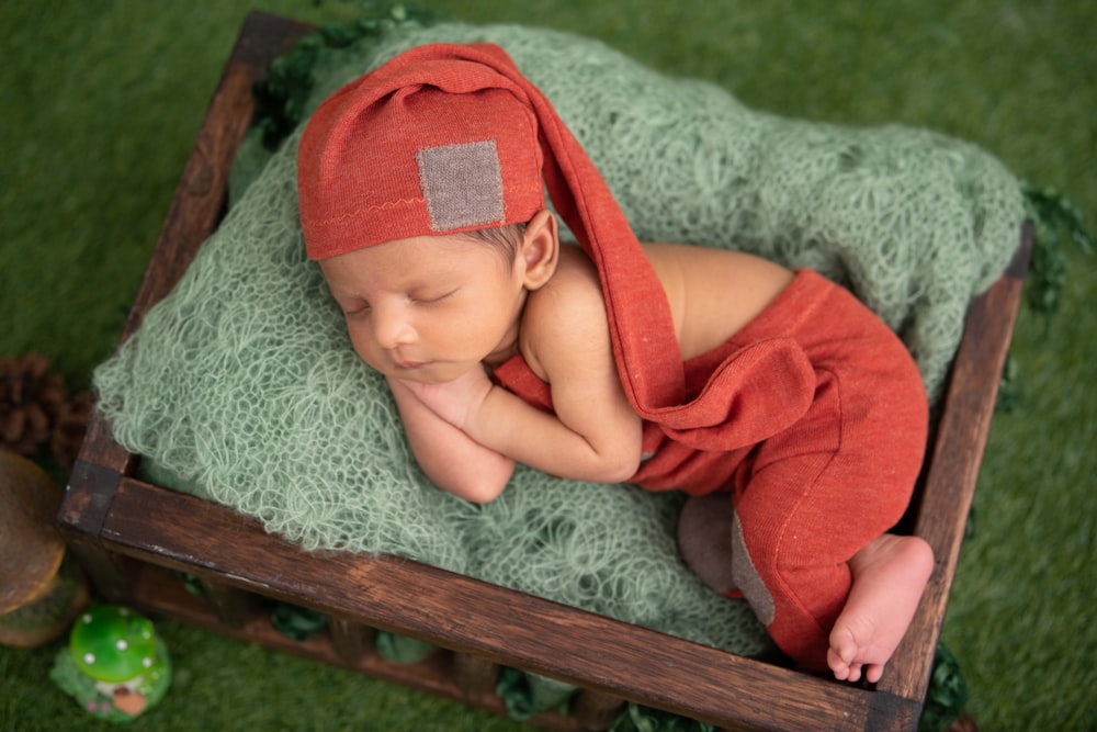 baby in red knit cap lying on gray textile