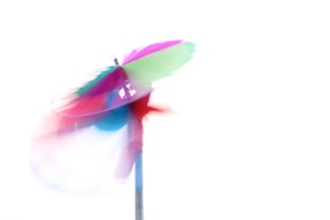 A vibrant, colorful pinwheel in motion against a stark white background, creating a sense of energy and playfulness. The bright colors blend seamlessly due to the motion blur, resulting in a dynamic and abstract visual.