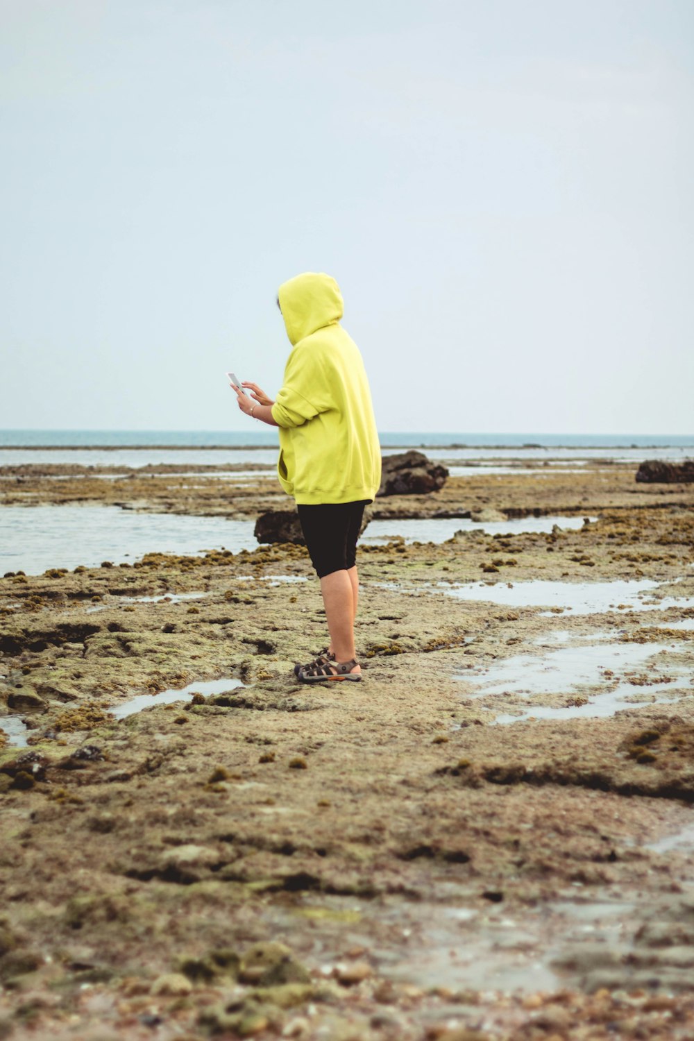person in yellow hoodie standing on beach shore during daytime