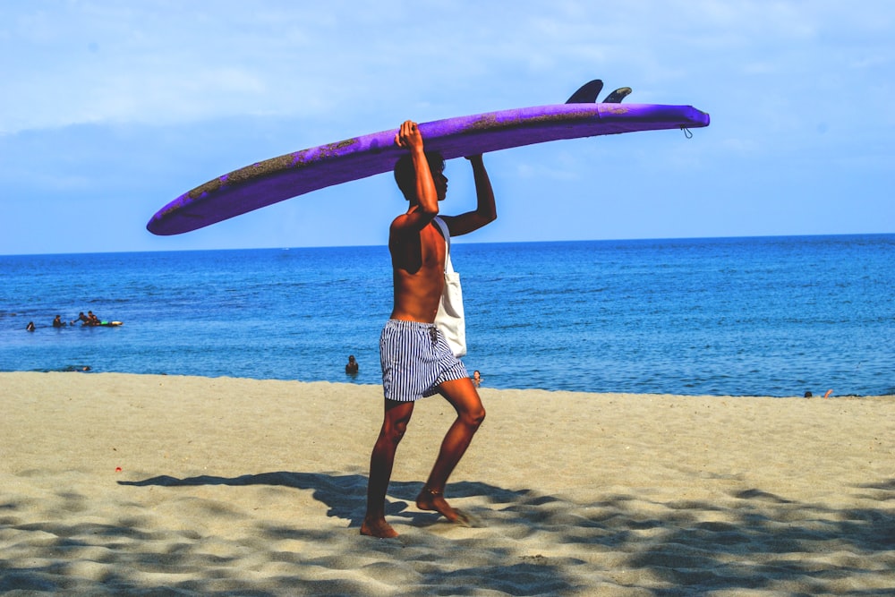 woman in white tank top and white shorts holding pink surfboard on beach during daytime