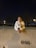 A person dressed in a white sweater is leaning on a concrete barrier, holding a soccer ball. It is nighttime, with streetlights illuminating the background, creating a calm and quiet ambience. Shadows are cast on the concrete wall, and the number 066 is stenciled on it.