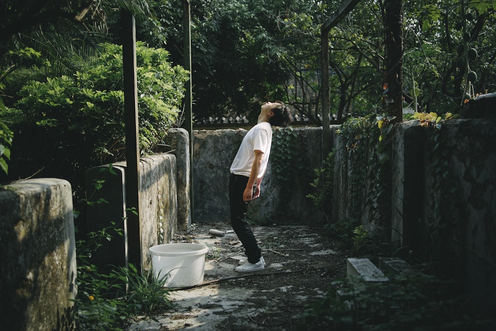 man in white t-shirt and black pants standing on gray concrete pathway