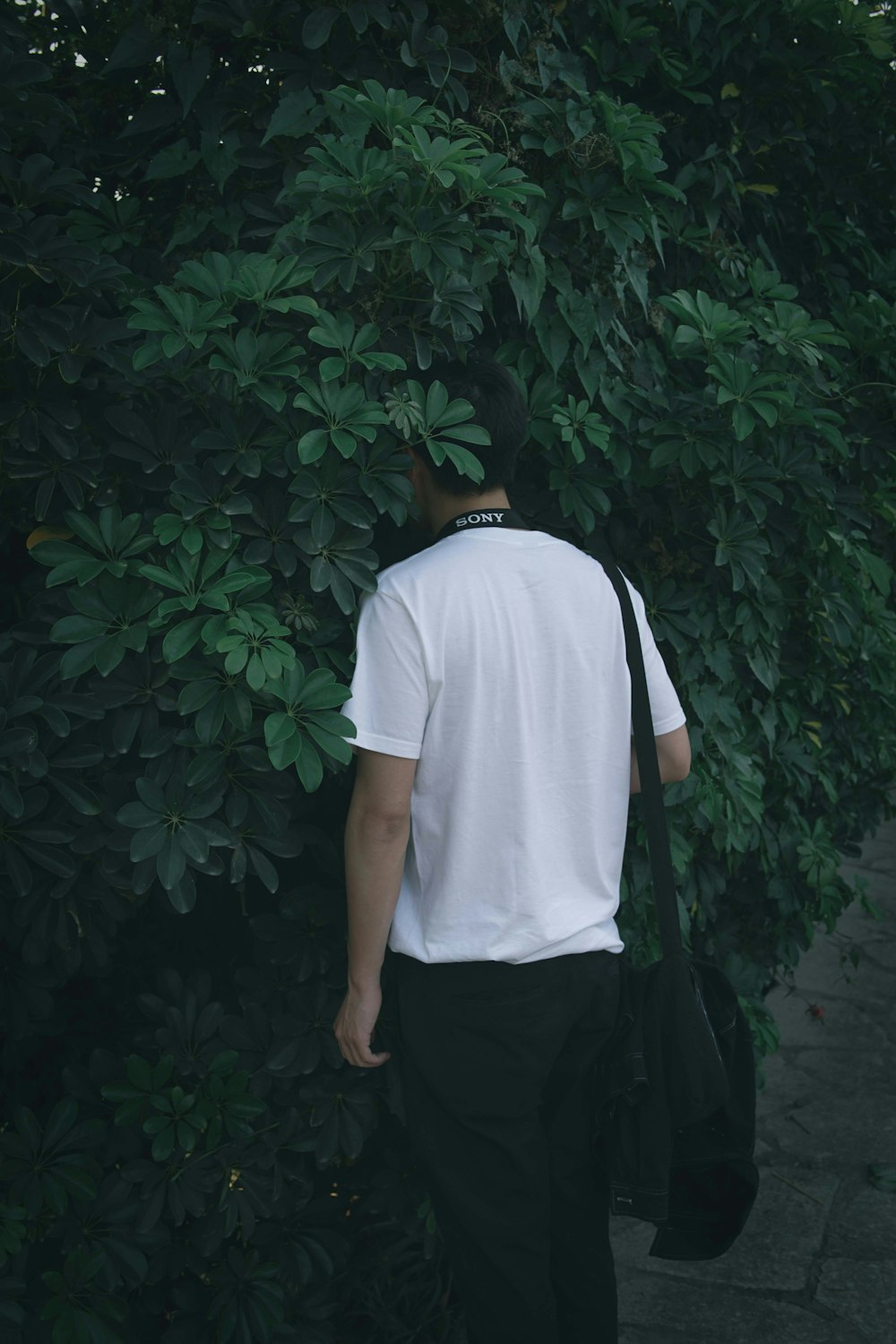 man in white t-shirt and black pants standing near green leaves