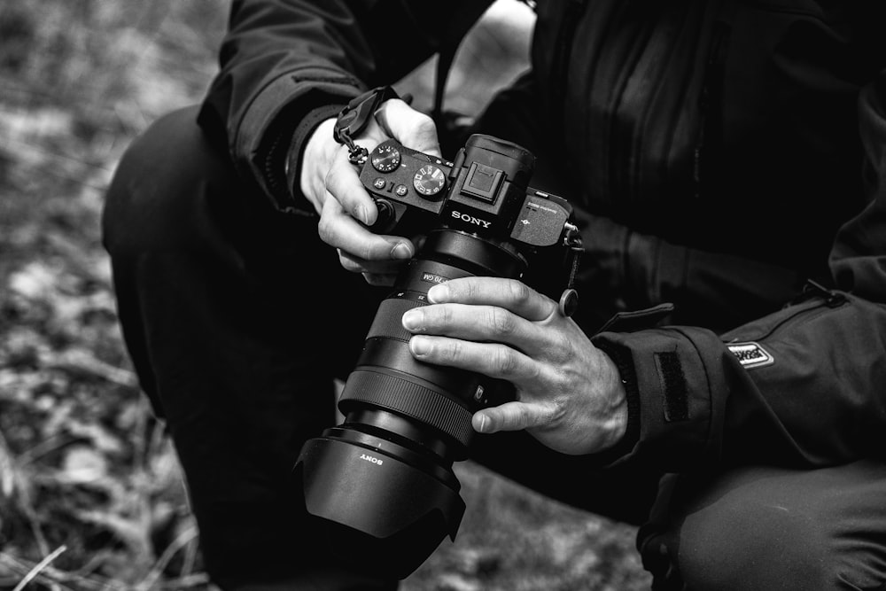 Photo en niveaux de gris d’une personne tenant un appareil photo reflex numérique