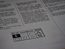 A printed page of text is visible, featuring instructions and explanations related to drawing tools and text editing. In the bottom section of the page, there is a graphic of a toolbox with various tool icons including a text tool and shape tools.