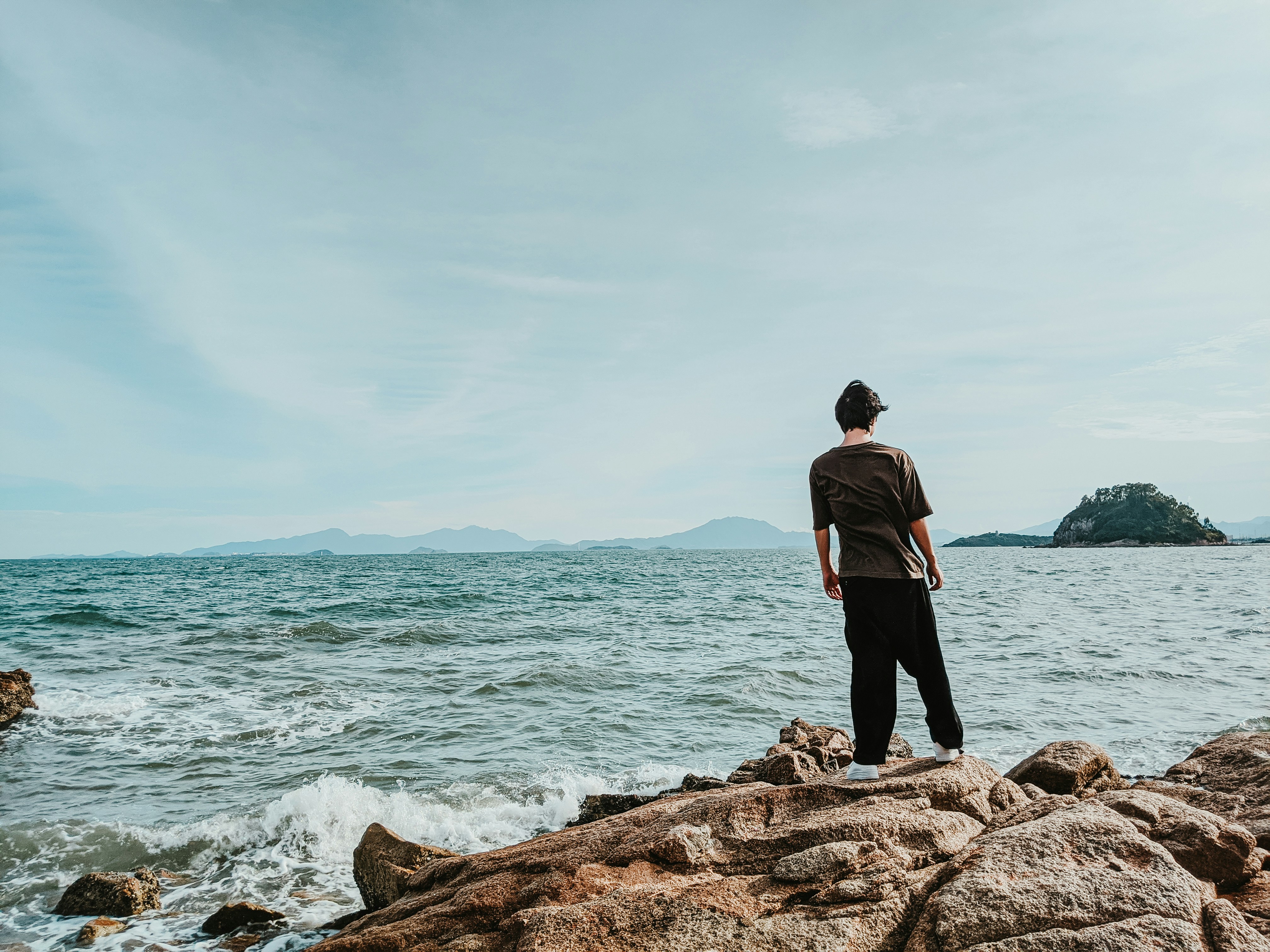 man in black jacket standing on brown rock near body of water during daytime