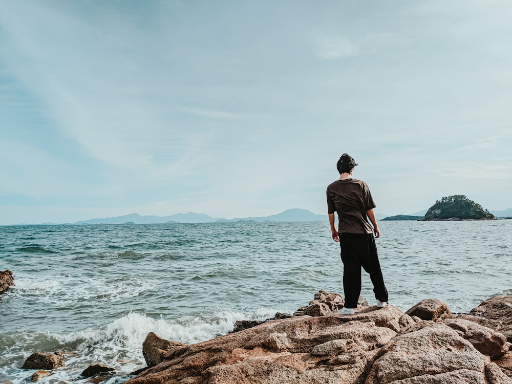 man in black jacket standing on brown rock near body of water during daytime