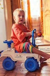 boy in red polo shirt sitting on white and blue plastic toy car
