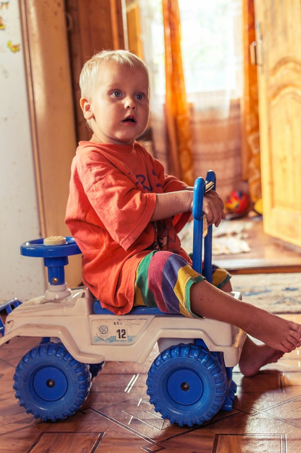 Niño en polo rojo sentado en coche de juguete de plástico blanco y azul