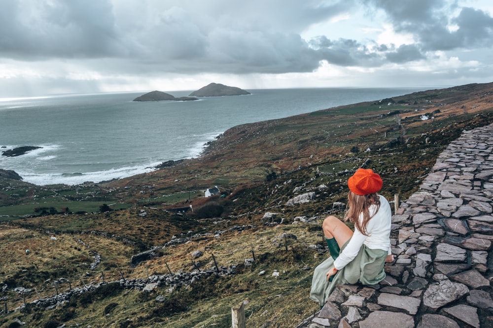 woman in white long sleeve shirt sitting on rock formation near body of water during daytime