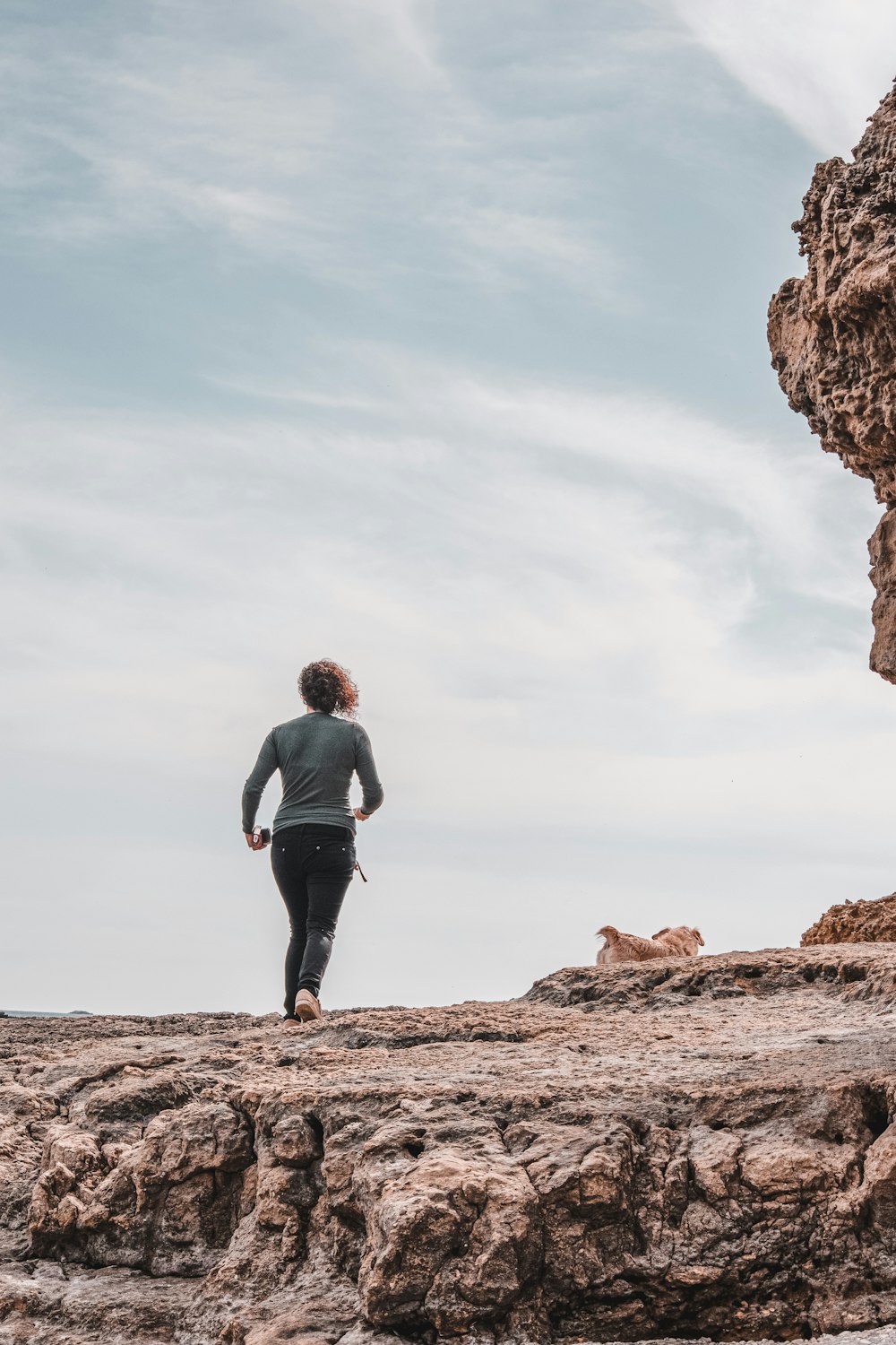 man in gray jacket and black pants standing on brown rock formation during daytime