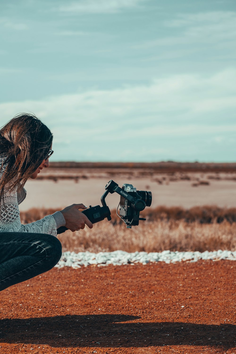 woman in white and black checkered dress shirt and blue denim jeans holding black dslr camera