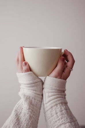 A hand wearing a cream-colored fleece-lined glove holding a warm mug.