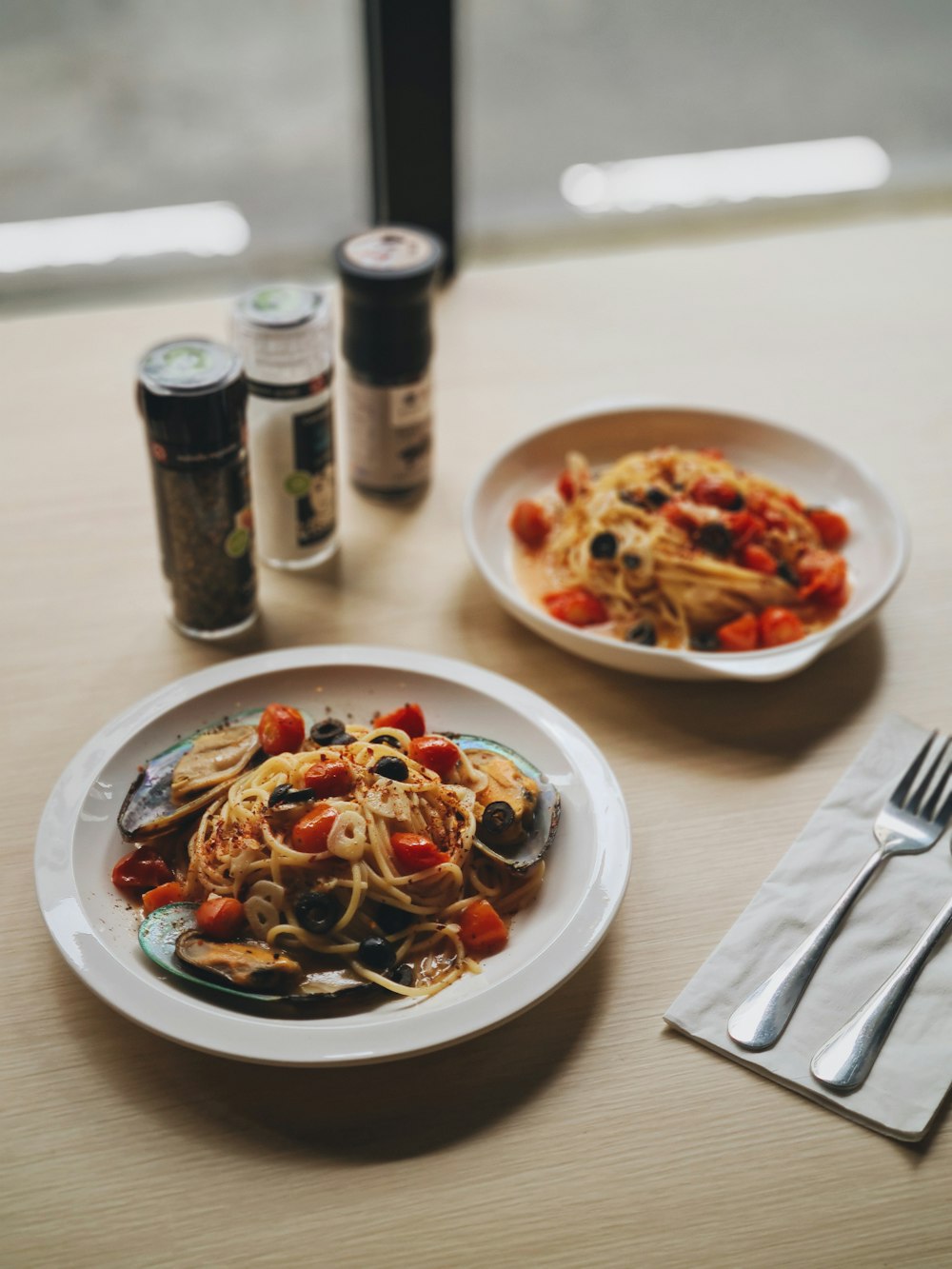 pasta dish on white ceramic plate beside stainless steel fork and knife