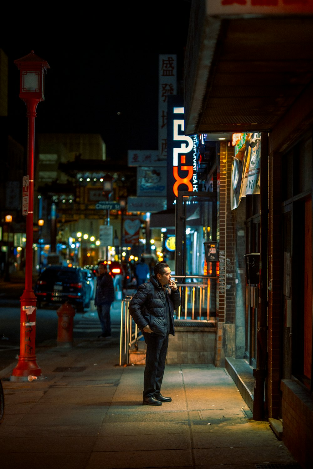 man in black jacket walking on sidewalk during night time