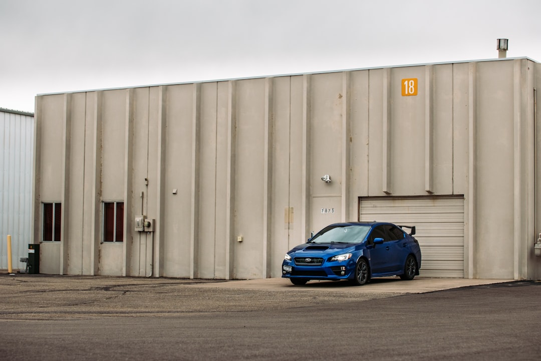 blue car parked beside gray steel wall