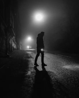 A shadowy figure standing beneath a flickering streetlamp on a foggy night.