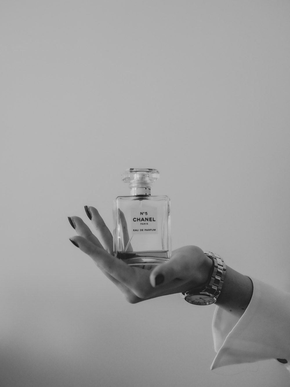 grayscale photo of person holding clear glass bottle