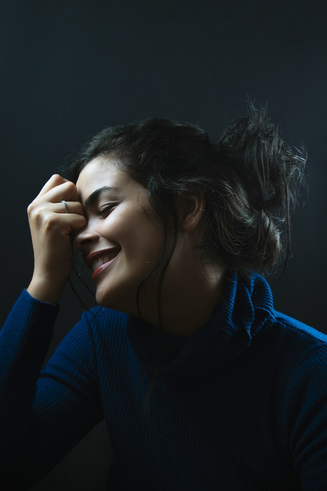 woman in blue sweater covering her face with her hands