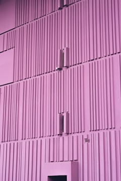 A minimalistic, vertically-aligned architecture with a purple hue. The facade features a repetitive pattern of rectangular ridges and protrusions, giving it a modern, geometric appearance.