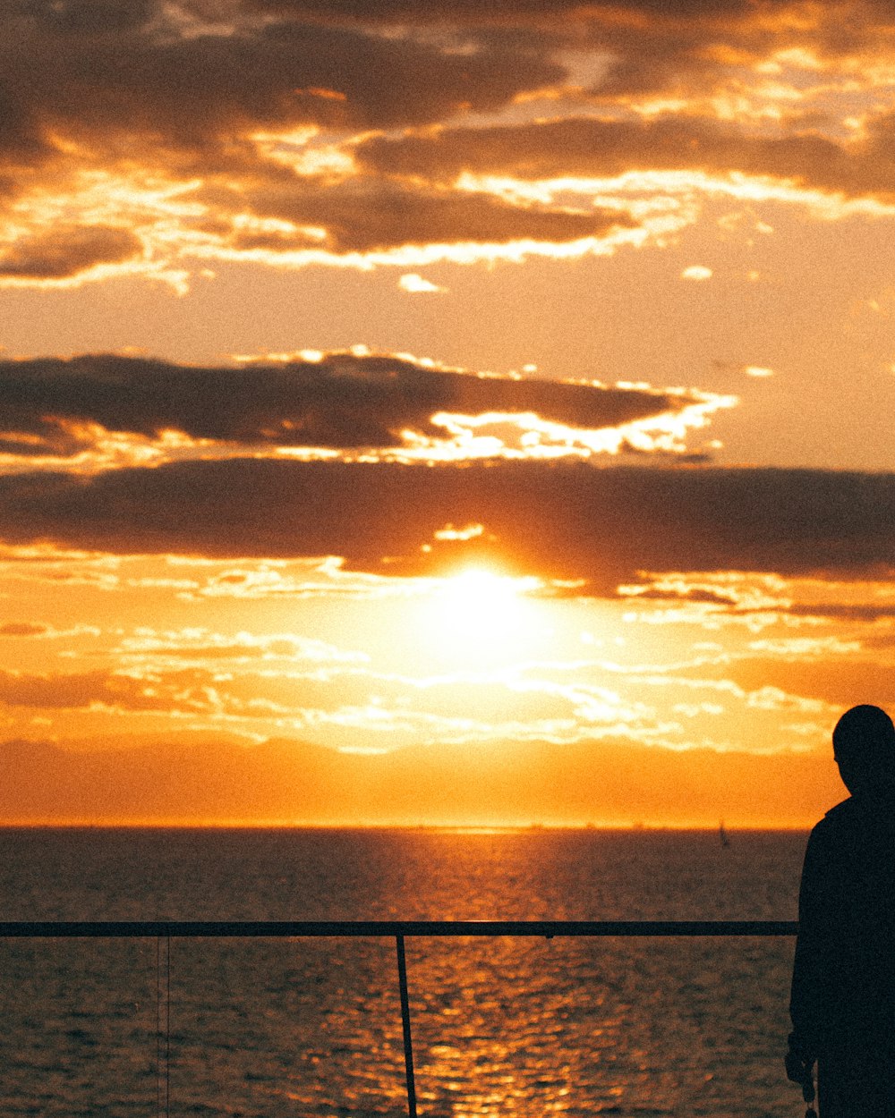 silhouette of man standing near body of water during sunset