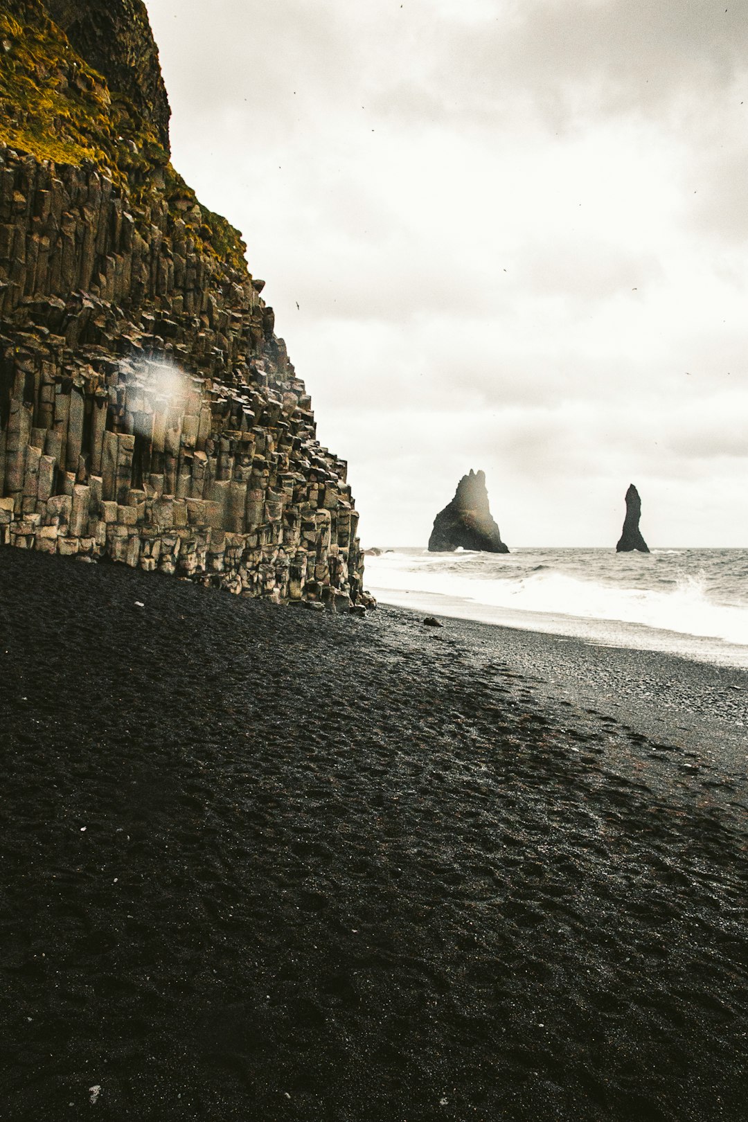 person walking on beach near rocky mountain during daytime