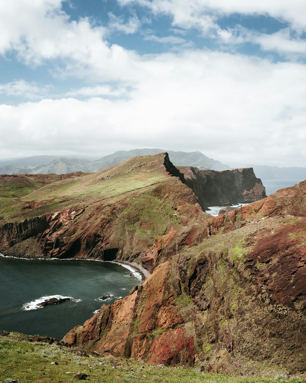 green and brown mountain beside body of water under white clouds and blue sky during daytime