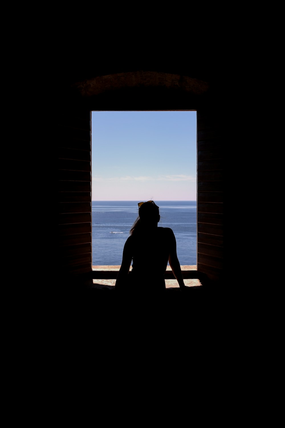 silhouette of woman sitting on window during daytime