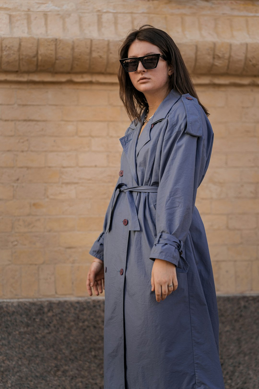 woman in blue trench coat standing on gray concrete floor during daytime