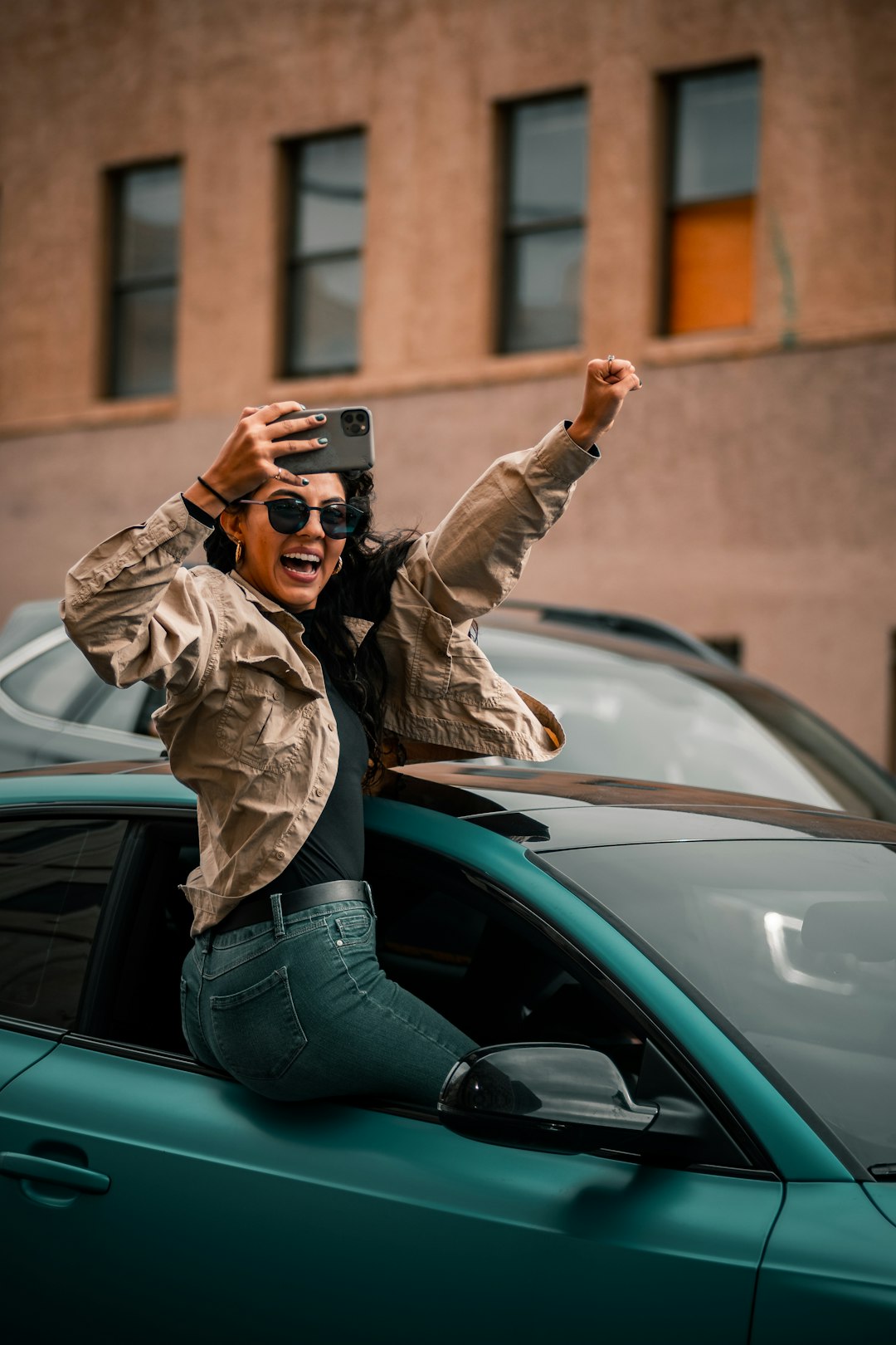 woman in brown jacket and blue denim jeans standing beside green car during daytime