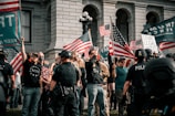 A still frame showing a protest rally with MAGA supporters holding flags.