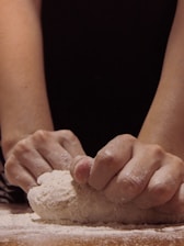 Close-up of a baker's hands shaping natural sourdough bread dough in a rustic kitchen.